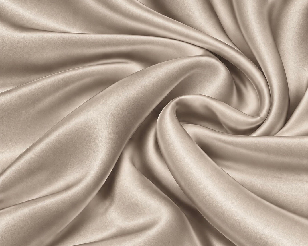 A close-up of draped satin fabric in a warm champagne beige color, arranged in elegant swirls that highlight its smooth texture and sheen.