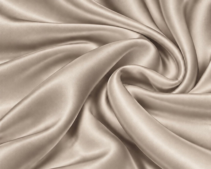 A close-up of draped satin fabric in a warm champagne beige color, arranged in elegant swirls that highlight its smooth texture and sheen.