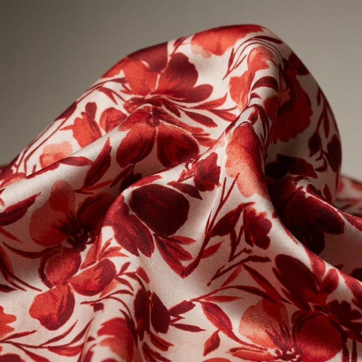 Close-up detail of red floral satin fabric’s micro-texture and vibrant print, captured with studio lighting.